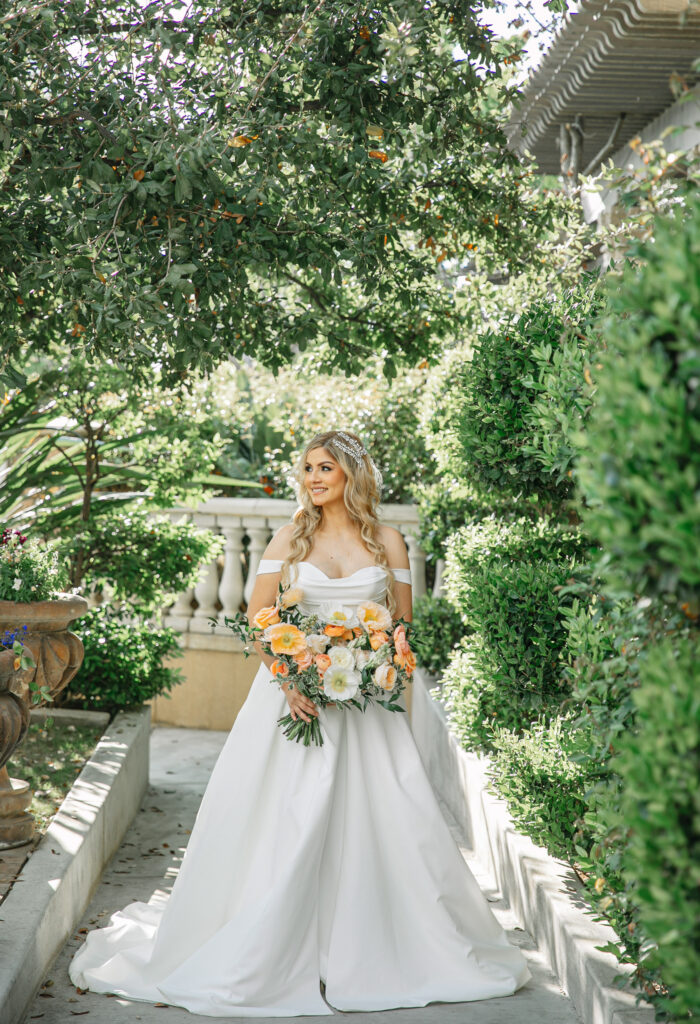 Bridal portraits surrounded by lush greenery in an Italian garden courtyard holding a bouquet for this spring wedding.