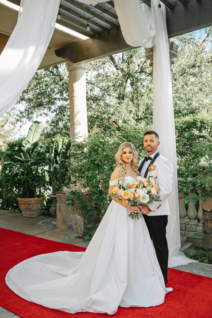 A couple takes their wedding portraits on the red carpet before their reception. Bride has a stunning bouquet of garden roses and poppies.