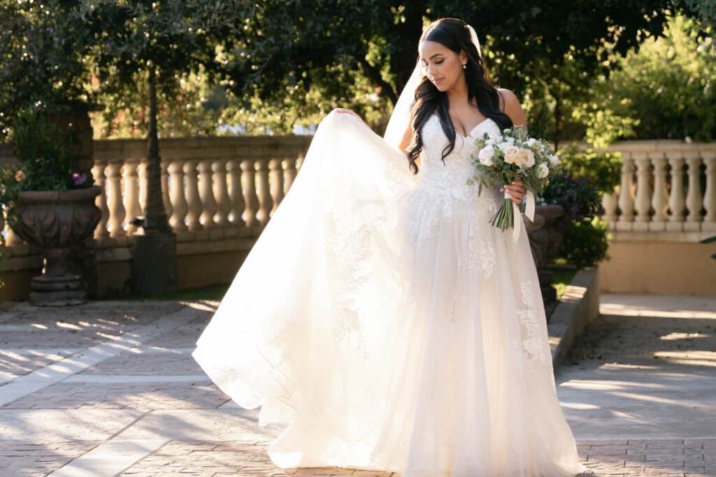 Bakersfield bride posing with her bouquet featuring ivory and white flowers in the garden courtyard of a Bakersfield Italian inspired indoor wedding venue.