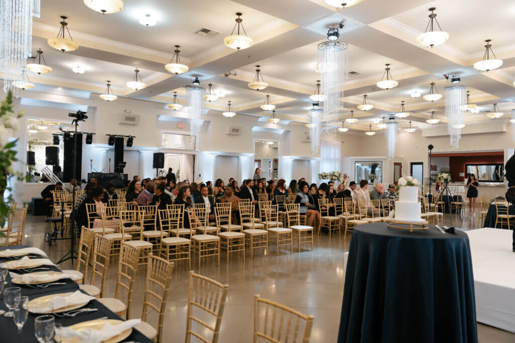 An indoor wedding venue features a ceremony setup while guests wait for it to begin.