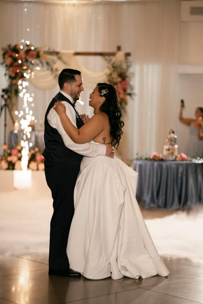 Wedding first dance in front of the sweetheart table adorned with colorful flowers. Cold sparks and low laying fog add to the romantic ambiance.
