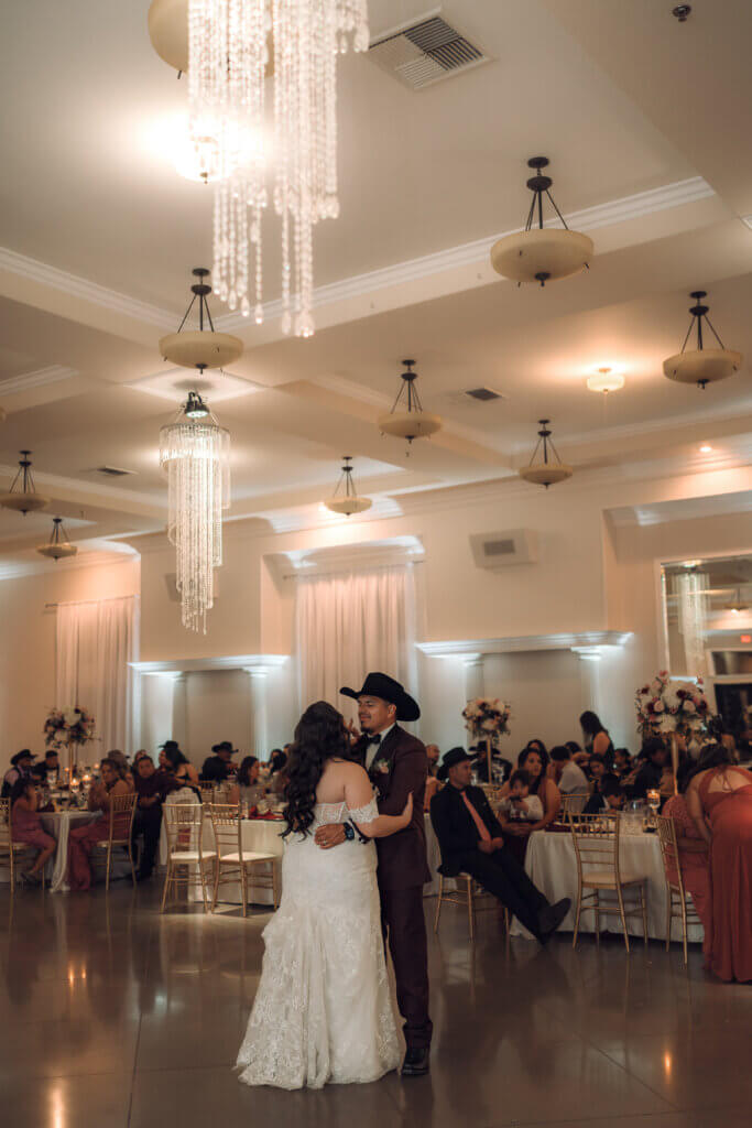 Bakersfield newlyweds having their first dance in an elegant wedding venue with tall ceilings and beautiful chandeliers. 