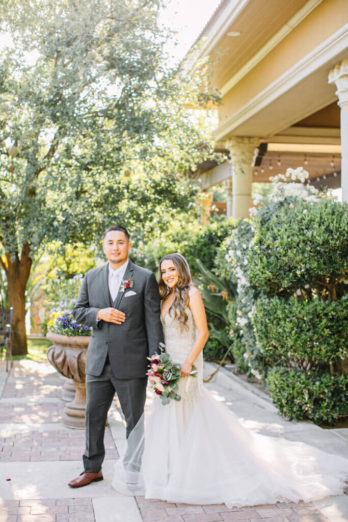 Bride and groom posing together for their wedding portraits in the garden surrounded by a manicured landscape.