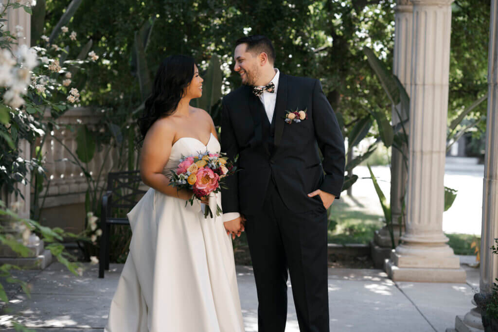 Bakersfield all-inclusive wedding package couple posing in the garden courtyard. Bride's bouquet features coral peonies, yellow ranunculus, with blue and burgundy accent flowers