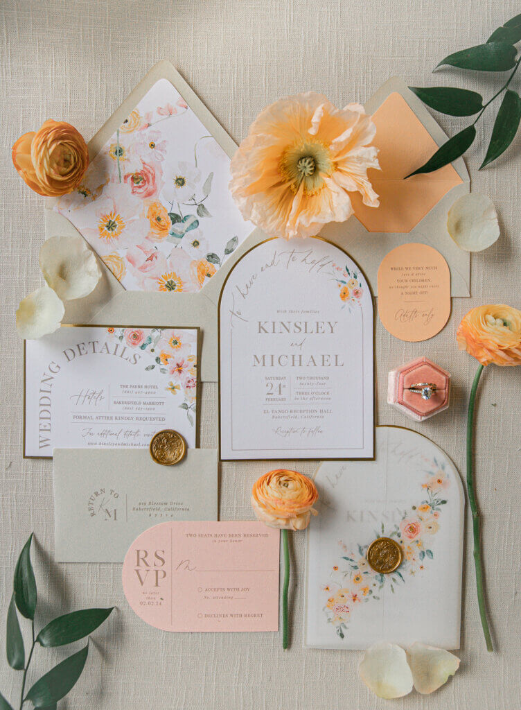 Wedding invitation flat lay styling featuring a spring wedding design with ivory, orange, and coral with ranunculus and a poppy.