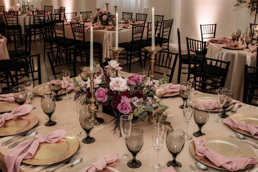 Moody bakersfield quinceañera guest table featuring tapere candles, smoky black water glasses and mauves, pinks, and burgundy flowers